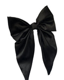 A large black satin hair bow clip with long tails lying on a white surface.