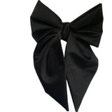 A large black velvet hair bow clip with long tails, placed on a white surface.