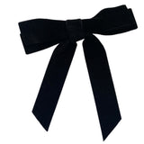 A double layered black velvet hair bow clip with long tails lying on a flat white surface, with a silver-colored barrette clip attached.