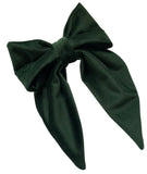 A bottle green velvet hair bow clip with long tails, displayed on a white background with daisies beside it.