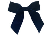A navy velvet hair bow with long tails with clip attached, placed on a white surface.