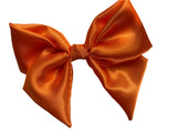 An orange  satin hair bow clip displayed on a white background, with a silver-colored barrette clip attached.