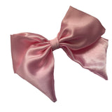 A baby pink satin hair bow clip displayed on a white background, with a silver-colored barrette clip attached.