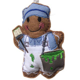 Gingerbread man decoration wearing a blue painter's outfit with green paint on his overalls, holding a paintbrush. On white background.