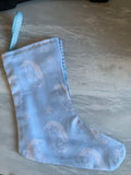 A light blue fabric Christmas stocking with a penguin pattern and a matching blue-and-white spot hanging loop, placed on a gray surface.