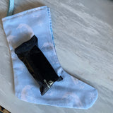 A light blue fabric stocking with a subtle tonal pattern and a blue patterned ribbon loop at the top, displayed on a gray marble surface.