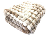A folded chunky blanket pram cover with a textured bobble pattern in cream, white, and light brown on a white background.
