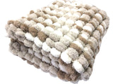 A folded chunky chenille blanket with a textured bumpy weave pattern in cream, beige, and light brown on a white background.