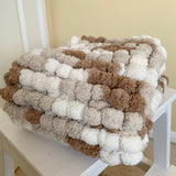 Blanket made of pom-poms on a white chair against a beige wall.