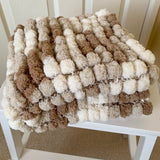 Textured blanket with brown and white pattern draped over a white chair.