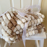 Pom-pom blanket in brown and white on a white chair with a white ribbon.