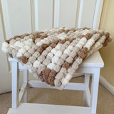 White wooden step stool with a textured brown and white blanket on top against a beige wall.