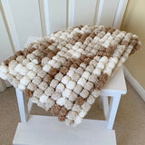 Textured blanket draped over a small white bench against a white wall.
