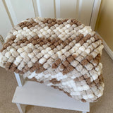 Blanket with brown and beige pattern on a white stool against a white wall.