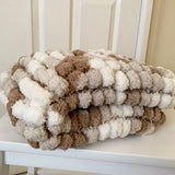 pom-pom blanket in brown and white on a white chair.