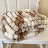 Textured blanket with brown, beige, and white pom-pom pattern on a white chair.