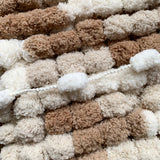 Close-up of regular and giant pom pom wool in brown, beige, and white for size comparison