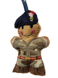 A handmade embroidered soldier ornament featuring a tan body, a dark blue beret with red, white, and gold embroidery, and a camouflage uniform with a red and yellow belt, hanging from a blue ribbon.