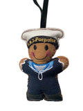 A handmade felt sailor ornament with a black ribbon hanger. The character has a brown felt face and arms, wearing a white sailor hat.
