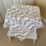 Textured blanket draped over a small white stool  against a neutral wall.