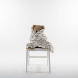 Teddy bear wrapped in a blanket sitting on a chair against a white background