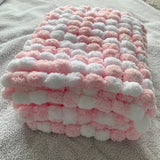 A folded plush blanket with a textured bumpy pattern in alternating pink and white sections, resting on a gray blanket background.