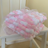A pink and white textured plush blanket wrapped in a sheer white ribbon, displayed on a white wooden chair in an indoor setting.