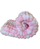 A rolled pink and white chunky pom-pom blanket pram cover.
