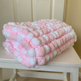A folded pink and white textured chenille blanket sits on a white wooden table in front of a cream-colored paneled door.