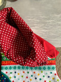 A hamdmade Christmas stocking with burgundy lining with white polka dots and a festive multicolour star and snowflake patterned front, shown folded on a light grey surface.