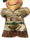 A close-up of a handmade embroidered fabric ornament with a tan face, pink cheeks, green hat, and a camouflage military-style outfit with a green belt, shown against a plain white background.