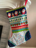A handmade Christmas stocking with a colorful pattern featuring Santa Claus, Christmas trees, wrapped gifts, and stars in multiple festive colours.
