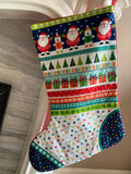 A Christmas stocking with a colorful pattern featuring Santa Claus, snow globes, Christmas trees, wrapped gifts, and stars in multiple festive colors.