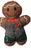 handmade gingerbread man fabric ornament on a plain light background. Dressed in a gray herringbone vest, green plaid kilt, and a red bow tie with a red rose accent.