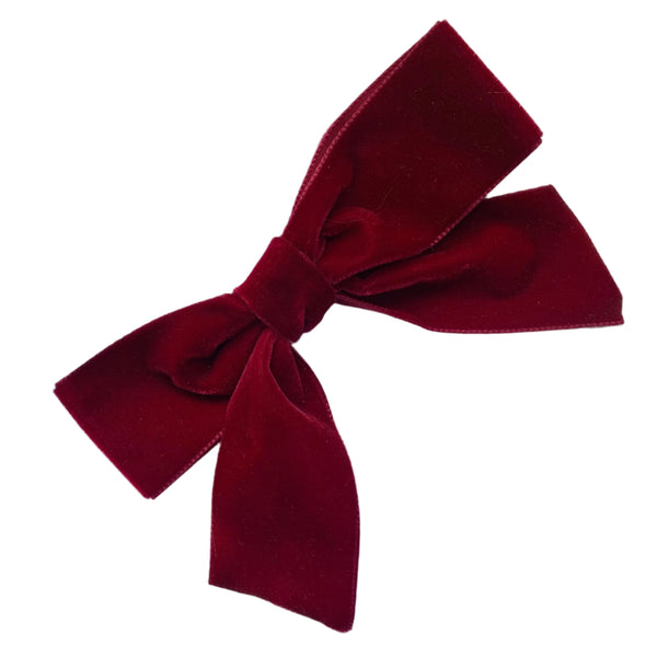 A dark red velvet hair bow clip laid out on a white surface.