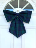 A large navy tartan door bow hanging on a white door
