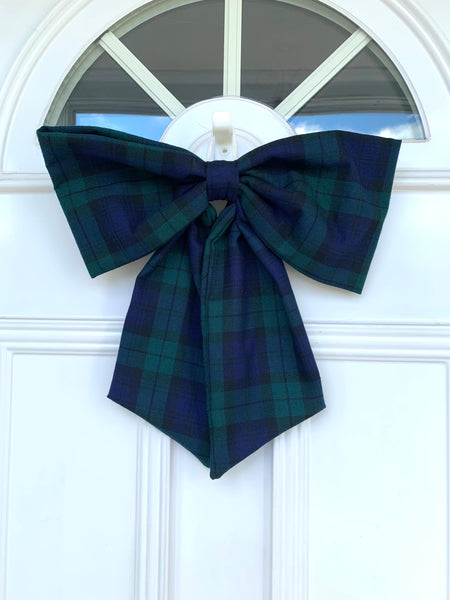 A large navy tartan door bow hanging on a white door