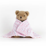 Teddy bear wrapped in a pink textured blanket on a white surface with a white wall background