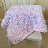 Pink and white hand knitted mini Pom Pom baby blanket draped over a white chair.