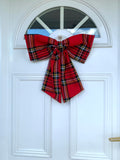 A large red tartan door bow attached to a white door, featuring a classic plaid pattern.