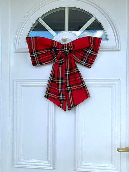A large red tartan door bow attached to a white door, featuring a classic plaid pattern.