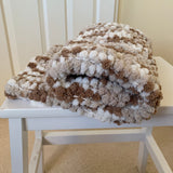 Textured blanket with brown and white pattern on a white chair