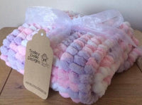 Pram baby blanket in shades of pink, purple and white. This chunky knit baby blanket cover is hand knitted in a super soft  pom pom wool.