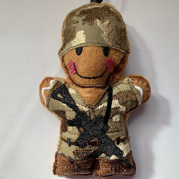 Gingerbread soldier felt decoration with gun.  in MTP machine embroidered fabric uniform and helmet and faux leather boots. Lightly filled and hand finished to create depth and character.