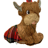 A felt decoration in the shape of an  highland cow with a red tartan kilt.