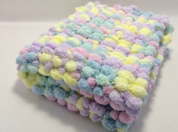 Pram baby blanket in pastel colours. This chunky knit baby blanket cover is hand knitted in a super soft  pom pom wool.