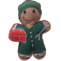 A gingerbread mannequin dressed in a green mechanic outfit with a smile on its face, holding a red toolbox.