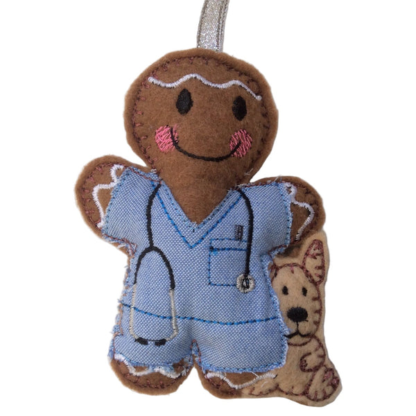 A gingerbread man veterinarian figurine with blue outfit and a dog figurine beside it, made of brown felt with embroidery details.