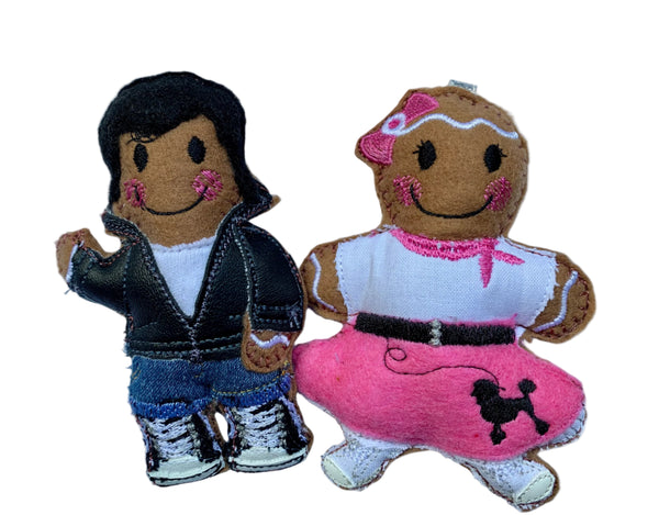 Two rockabilly style gingerbread decorations. Male version is dressed in black leather jacket, jeans and baseball shoes, female dressed in 50s style pink circle skirt with white top and pink neckscarf. on white background.