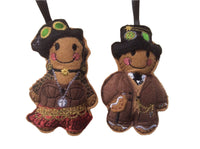 Two felt gingerbread man and woman decorations in steampunk fashion, with decorative details such as hats and chains, designed as ornaments.